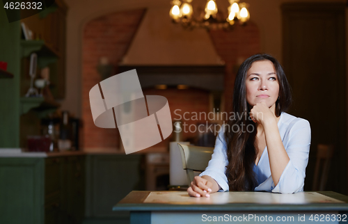 Image of Serious staying at home woman sitting at the table