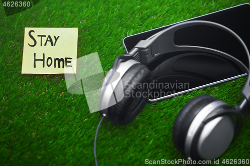 Image of Stay Home text on sticky note on a grass with headphones and dig