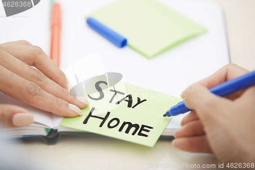 Image of Hands of woman writing on adhesive note with Stay Home text