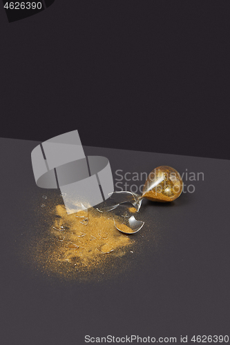 Image of Crashed outdated hourglass with golden sand on a black duotone background.