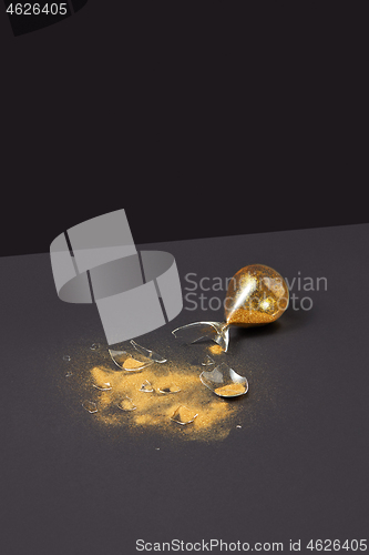 Image of Broken antique sandglass with golden sand on a black duotone background.