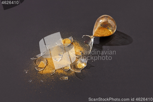 Image of Crashed sandglass with golden sand on a black background.