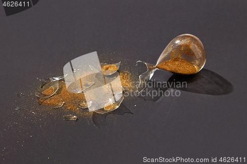 Image of Broken antique hourglass with golden sand on a black background.