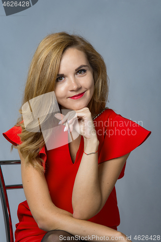 Image of Cute girl in beautiful red dress sits on a chair