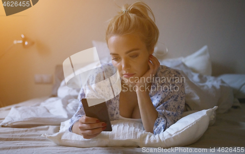 Image of Lovely young woman with cute ponytail lying on comfortable bed and browsing smartphone