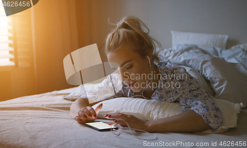 Image of Charming young woman with ponytail listening to good music while lying on comfortable bed