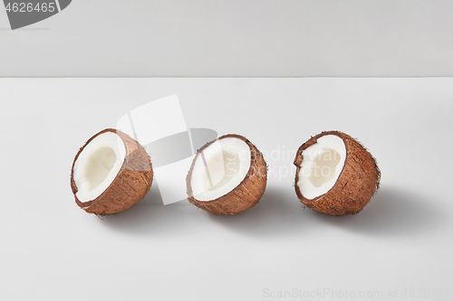 Image of Three halves of fresh ripe organic coconut on a light grey background.