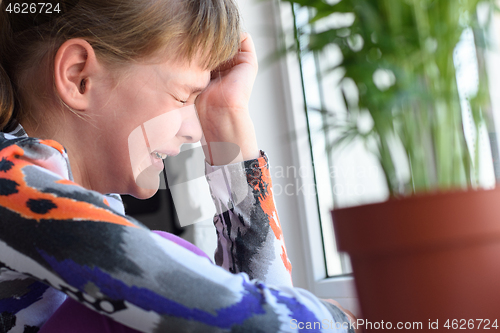 Image of Ten year old girl sobs at the window in the room