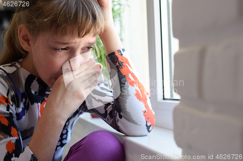 Image of Girl weeping bitterly at the window wipes her tears with her hand