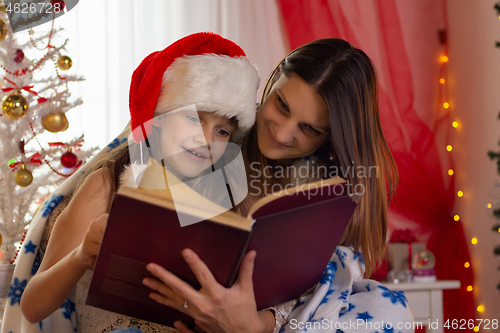 Image of Girl with child reading a book in a decorated christmas room