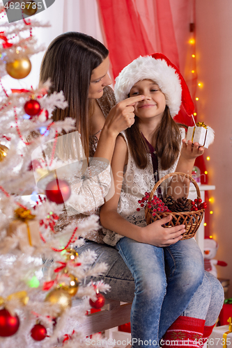 Image of Mother touches her daughter\'s nose dressed in Christmas attire near a Christmas tree