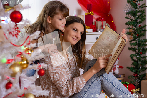 Image of Mom and daughter read a book near a Christmas tree