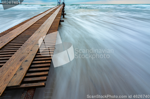 Image of Wooden pier stretching into the distance, surf with blurry waves