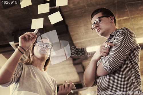 Image of young couple at modern office interior writing notes on stickers