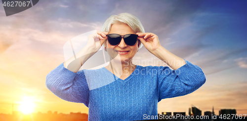 Image of senior woman in sunglasses over sunset in city