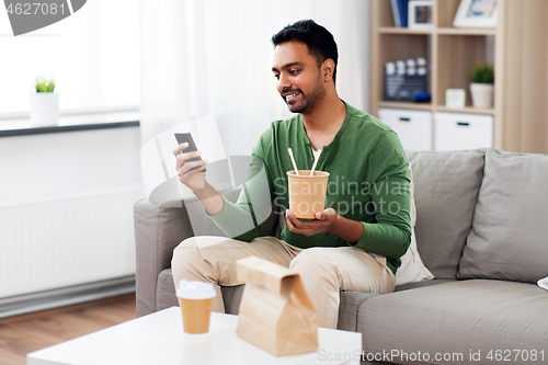 Image of smiling indian man eating takeaway food at home