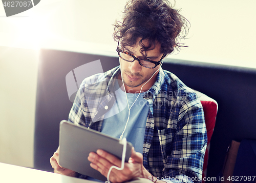 Image of man with tablet pc and earphones sitting at cafe