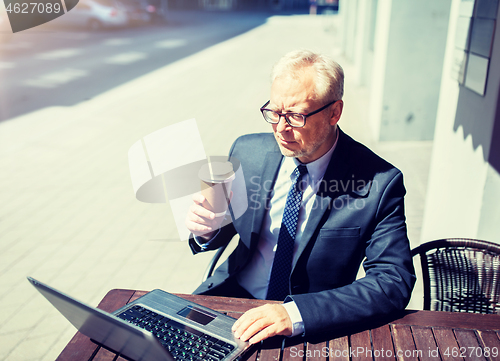 Image of senior businessman with laptop drinking coffee