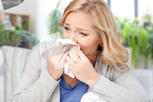 Image of ill woman blowing nose to tissue at home