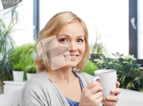 Image of smiling woman with cup of tea or coffee at home