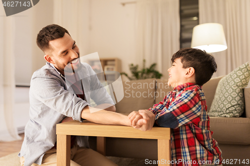 Image of happy father and little son arm wrestling at home