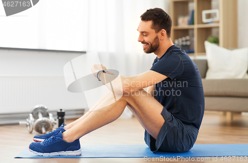 Image of smiling man with fitness tracker exercising at home