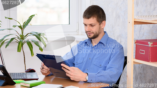 Image of Office worker at the table reads documents in a folder