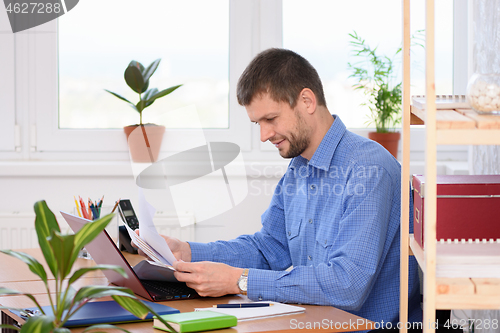 Image of Successful young man reads documents while sitting at a table in the office
