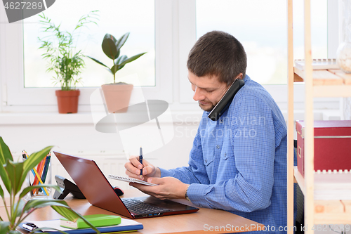 Image of Businessman talking on the phone and taking notes in a notebook