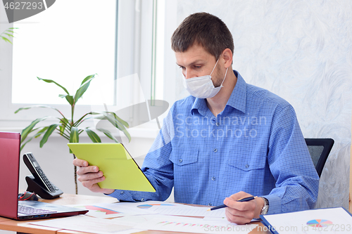 Image of An office employee communicates in a tablet by video link, a medical mask is on his face