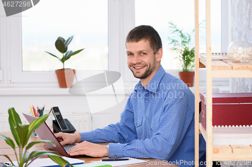 Image of Successful young man in the office works in the computer and looked into the frame