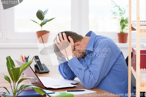 Image of Office employee clutching his head in his hands while reading a document.