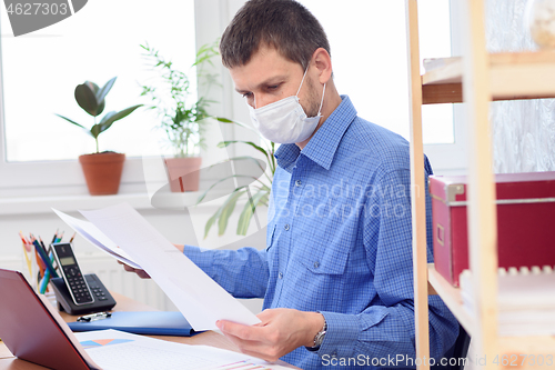 Image of Office worker in protective medical mask works with documents in the office