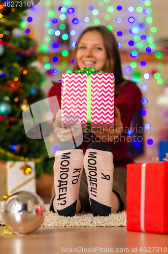 Image of a happy girl in funny socks with the inscription \"who\'s good? I\'m good!\" with a big gift in the background of Christmas lights