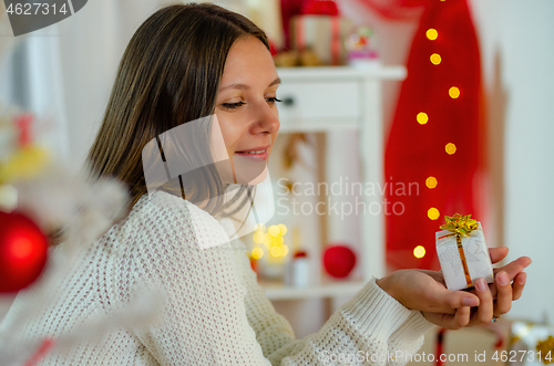 Image of Beautiful young girl looks tenderly at the gift in the decorated Christmas room