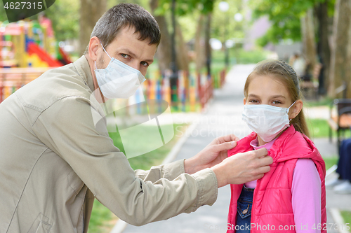 Image of Dad on the street puts on his daughters face a medical mask, looked into the frame