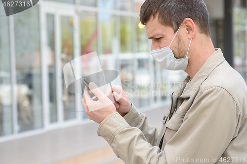 Image of A man in a medical mask dials a number in a mobile phone, close-up