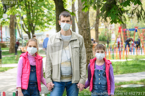 Image of Dad and two daughters are in protective medical masks at the playground