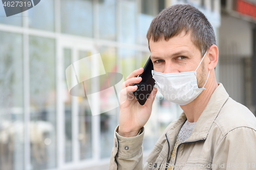 Image of Portrait of a man in a medical mask with a mobile phone on the background of the store, looking in frame