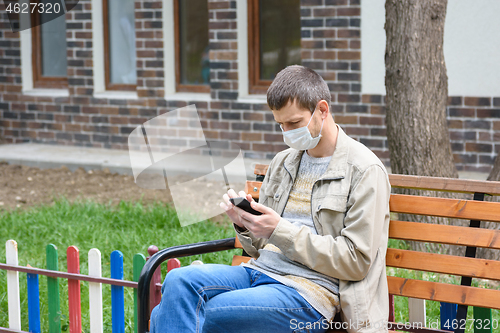 Image of A man on the street crouching on a bench looks at the phone screen