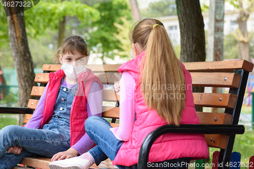 Image of Girlfriends with face masks talk while sitting on a bench in the playground