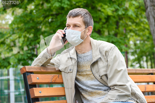 Image of A man in a medical mask is talking on the phone in a park