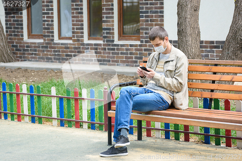 Image of A man in the isolation mode walks on the street and crouches on a bench, looks at the phone screen