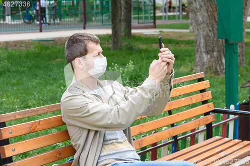Image of A man in a medical mask is photographed on the phone