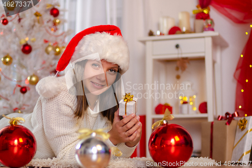 Image of Happy girl in Christmas dress lies on the floor near the Christmas tree with a gift