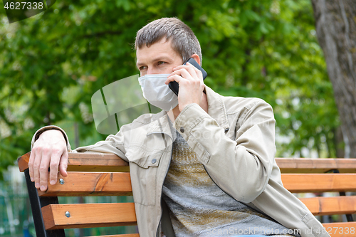 Image of A man sits on a bench in a medical mask and talks on the phone