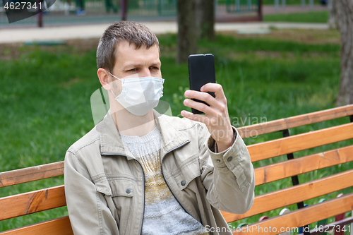 Image of A man in a medical mask sits on a bench and photographs himself