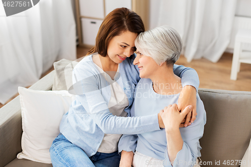 Image of senior mother with adult daughter hugging at home