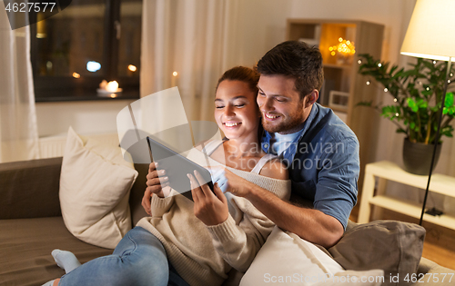 Image of happy couple using tablet pc at home in evening