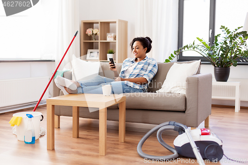 Image of woman with smartphone resting after home cleaning